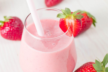 Glass of fresh strawberry milkshake, smoothie and fresh strawberries on pink, white and wooden background. Healthy food and drink concept.