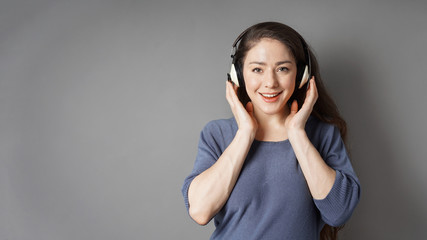 happy smiling young woman listening to music with wireless headphones - gray background with copy...