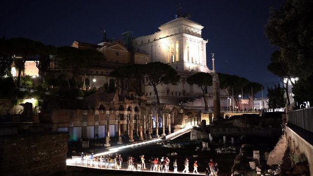 Beautiful night cityscape of Rome, ancient illuminated Piazza Venezia and crowded streets. People walking along Fuori Imperiali street, taking photos of Rome at night. Illuminated path for tourists