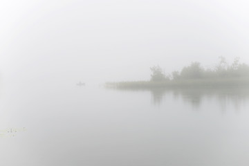 Fisherman on a boat fishing on a lake on a foggy morning