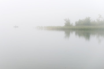 Fisherman on a boat fishing on a lake on a foggy morning