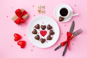 Valentine's day breakfast. Heart made of chocolate candies, gift with a red bow and cu of coffee on  a pink background
