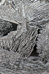 Crystals of frozen water close-up. Ice and frost on a window pane in winter. Abstract pattern. Weather forecast: frost, cooling. Dark background or wallpaper. The picture is monochrome. Vertical shot