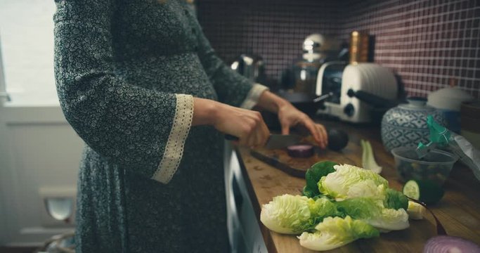 Pregnant woman in kitchen making salad and cutting onions