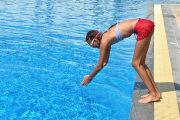 Child girl dives into the pool. Girl learning to swim autdoor. Swimming pool in the hotel. Children swim in the outdoor pool.