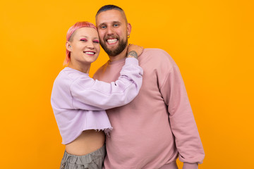 happy smiling couple of girl and guy with colored hair and piercing are standing in an embrace on a yellow background