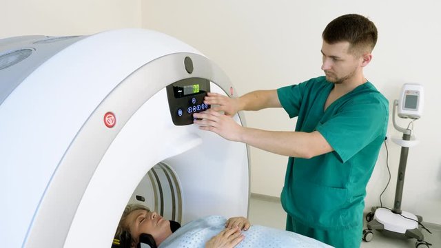 Professional radiologist controls CT or MRI or PET scan with elderly female patient undergoing procedure. Doctor conducts medical checkup with advanced technologies in medicine. 4K