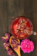 dried pink roses and tea in glass on black wood background, dry rose petala in wood spoon