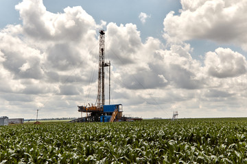 Drilling rig against the blue sky in a corn field