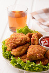 Chicken nuggets with ketchup and lettuce in a plate on a white wooden background. Vertical shot