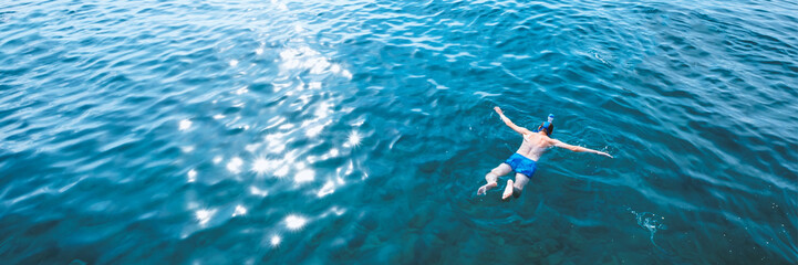 Young man in swimwear lying on blue water. Man in swimming mask relaxing in sea. Tropical summer...