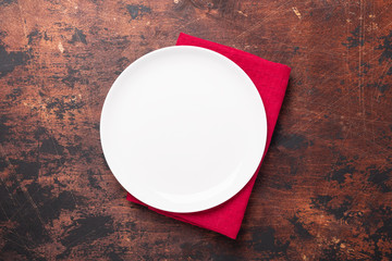 Empty ceramic white plate and red linen napkin on brown wooden background Copy space Top view