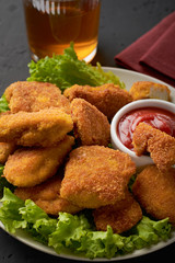 A plate of cooked chicken nuggets with ketchup and a glass of beer on a dark background. Vertical frame