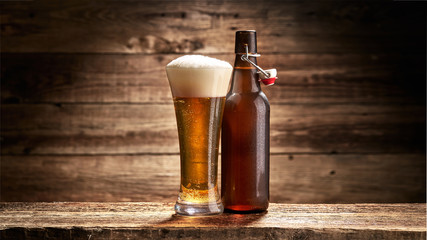 Szklanka pełna piwa i butelka na tle starych desek