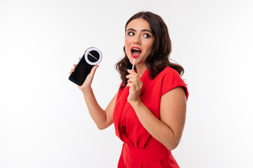 Obraz premium charming brunette Caucasian young woman video blogger shoots video on the phone with a flash device on a white background