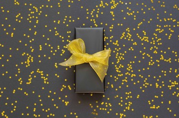 Festive background , gift box with shiny golden ribbon on a black background with glitter gold stars , flat lay, top view