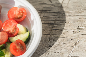 Salad of red tomatoes and green cucumbers with sausage are on plastic plate.