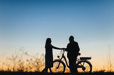 Fototapeta na wymiar Male cyclist on the e-bike or electric bicycle on the sunset background. Silhouette of the man and girl in profile. Active pension. Travel. Sport.