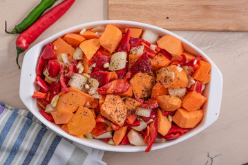 Sliced sweet potato with onions and carrots in a baking dish on the table