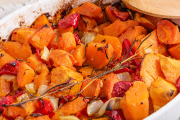 Baked sweet potato with onions and carrots, spices and sprigs of rosemary in a baking dish on a table close-up