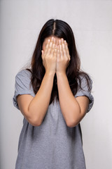 Young asian woman hides her face, studio photo on gray background. social phobia problem concept.