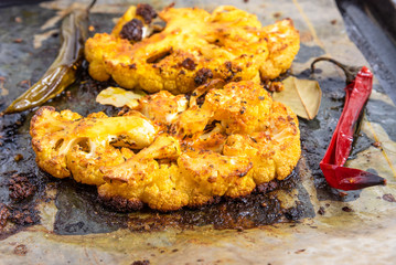 Baked cauliflower steaks sprinkled with spices on a baking sheet with chili peppers, close-up