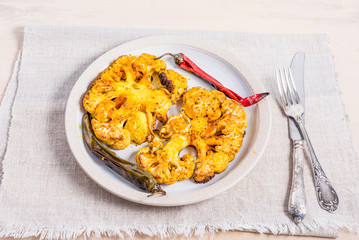 Baked cauliflower steaks sprinkled with spices on a plate with chili peppers, top view