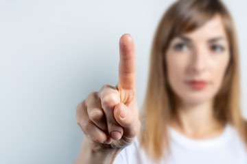 Young woman touches or pushes a finger at something on a light background