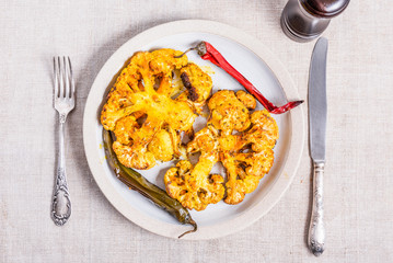 Baked cauliflower steaks sprinkled with spices on a plate with chili peppers, top view