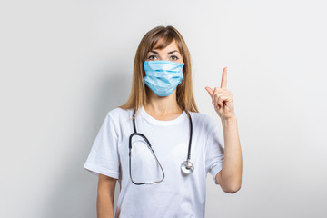 Young woman in medical mask and stethoscope pointing finger on a light background. Banner. Concept doctor, high level medical medicine, vaccination, visit to the doctor