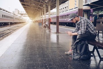 Young man using mobile smart phone checking train timetable at train station platform. Asian...