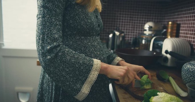 Pregnant woman in kitchen chopping salad