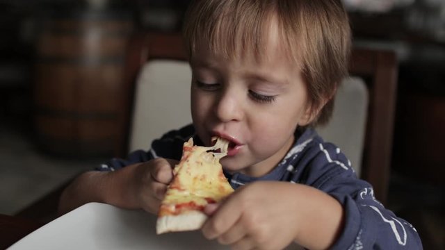 Close up of little cute boy eating pizza. Neutral colors for collor correction.