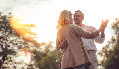 Senior active caucasian couple dancing and holding hands looks happy in the park in the afternoon autumn sunlight,bokeh,anniversary,happily retired with copy space.Concept health insurance