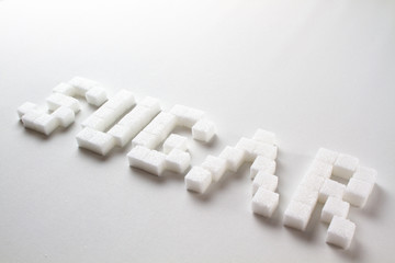 "Sugar" spelled with pixel art letters made out of sugar cubes on a white background