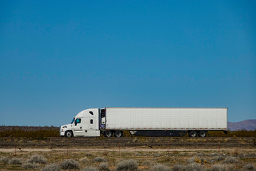 CLOSE UP: White semi-trailer truck hauls a container across a desert in the USA. © helivideo
