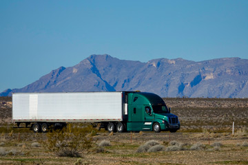 CLOSE UP: Cool shot of barren landscape surrounding a green semi-trailer truck.