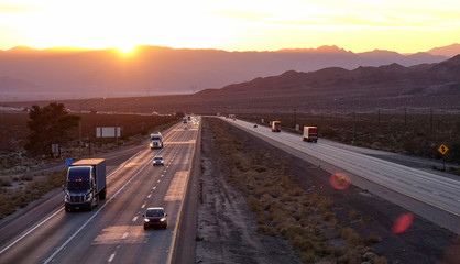 AERIAL: Scenic shot of 18 wheeler trucks and cars crossing Mojave desert at dusk