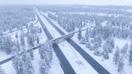 AERIAL: Scenic drone view of white snowy landscape surrounding a busy highway.