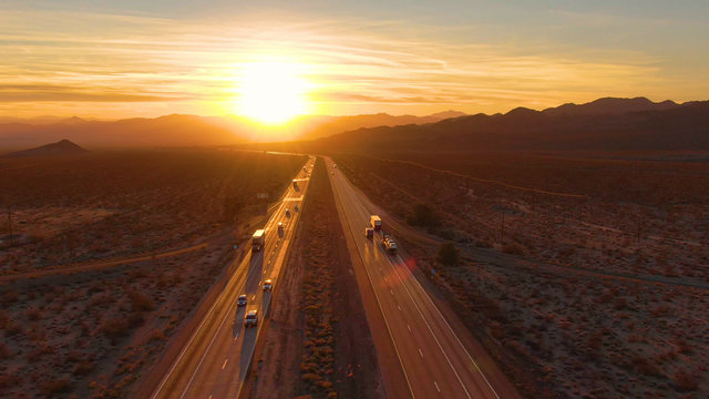 DRONE: Scenic shot of 18 wheeler trucks and cars crossing Mojave desert at dusk