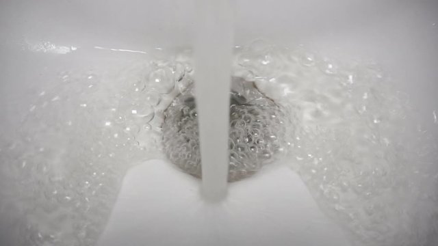 A stream of water flows in a white sink pouring into a pit with a shiny stainless steel grill close-up.1920 X 1080 Full Hd.