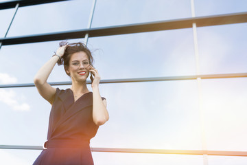 girl business woman in a sleeveless suit talking on the phone against the background of a glazed business center building