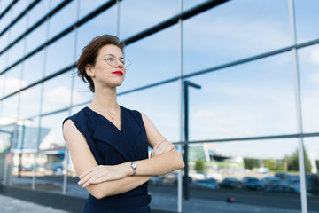 Fototapeta premium successful business woman posing against the backdrop of a mirror building with reflection of clouds and sky