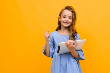 girl in a beautiful dress of delicate blue color with a tablet in hand on a yellow background with copy space