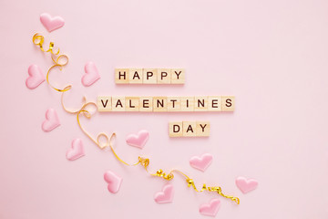 Confetti heart on a pink pastel background with wooden letters. Valentine's day greeting card concept. Top view, flat lay, copy space.