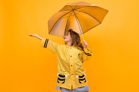 happy joyful girl in a beautiful yellow raincoat in the image of a bee holds a silver umbrella and extends her hand on a yellow background