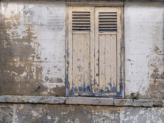 old concrete wall with crumbling white paint and old windows with the shutters closed