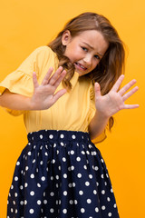 girl in a t-shirt and skirt waving her arms in displeasure and denies on a yellow background