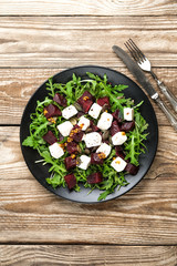 Obraz na płótnie Canvas Salad with beetroot, feta cheese, arugula and spicy dressing on a rustic background. Healthy food. Top view. Copy space.