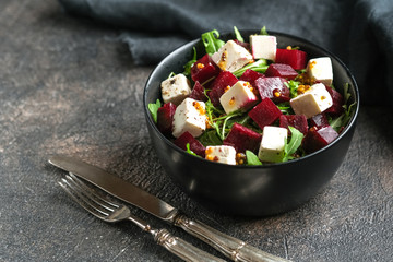 Salad with beetroot, feta cheese, arugula and spicy dressing on a dark background. Healthy food. Top view. Copy space.